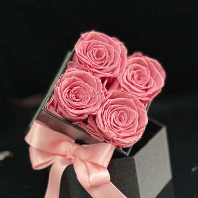 Four pink roses in a black gift box with a pink ribbon