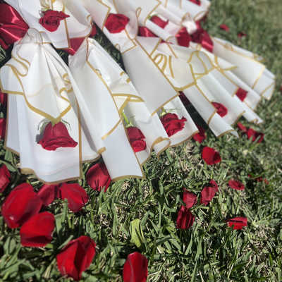 Red roses wrapped in white paper with gold trim and red ribbons on grass