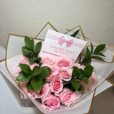 Bouquet of pink roses wrapped in white paper with green leaves