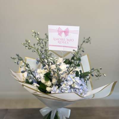 Bouquet of pale blue and white flowers wrapped in white paper with a ribbon