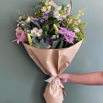 Hand-tied bouquet of mixed pink, white, purple, and yellow flowers in kraft paper