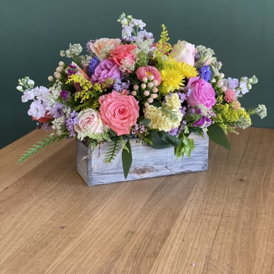 Mixed pink and purple flower arrangement in a wooden box
