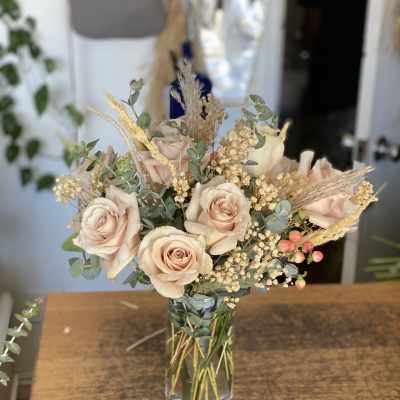 Blush roses arranged in a clear glass vase with dried grasses and filler flowers.
