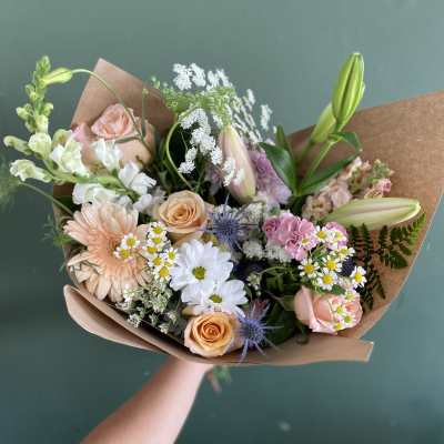 Handheld bouquet of pastel flowers wrapped in brown paper