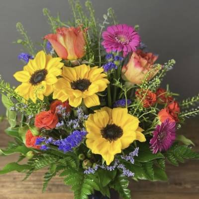 Colorful bouquet of sunflowers, roses, and gerbera daisies in a dark vase