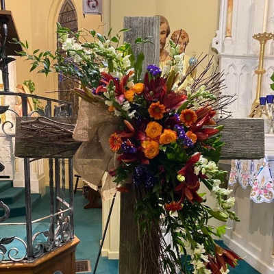 Large floral cross arrangement with orange, red, white, and purple flowers