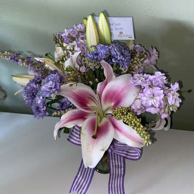 Pink lilies and lavender flowers in a glass vase with a striped ribbon