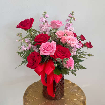 Bouquet of red and pink roses in a textured vase with a red ribbon