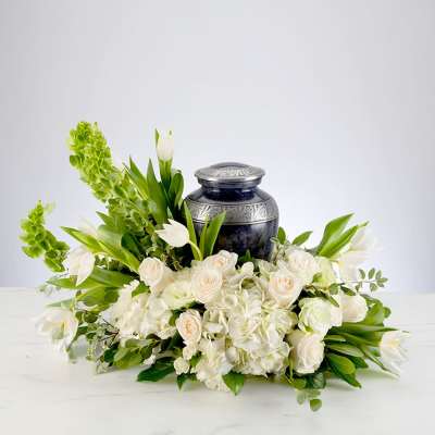 Cremation urn surrounded by white roses, hydrangeas, tulips, and Bells of Ireland in a low arrangement
