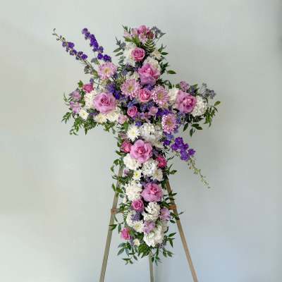Cross-shaped floral arrangement with pink, white, and purple flowers on an easel