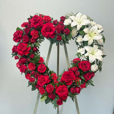 Heart-shaped floral wreath with red roses and white lilies on an easel