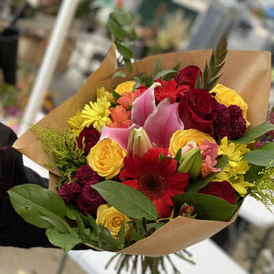 Mixed bouquet of roses, lilies, and daisies wrapped in brown paper