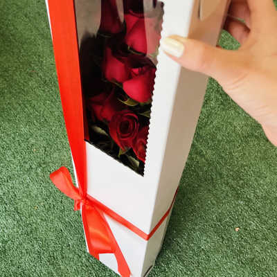 Boxed red roses with a red ribbon on a green surface