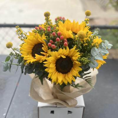 Bouquet of sunflowers with pink berries and eucalyptus in kraft paper