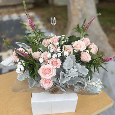 Pink roses arranged with white filler flowers and silver foliage in a wrapped bouquet