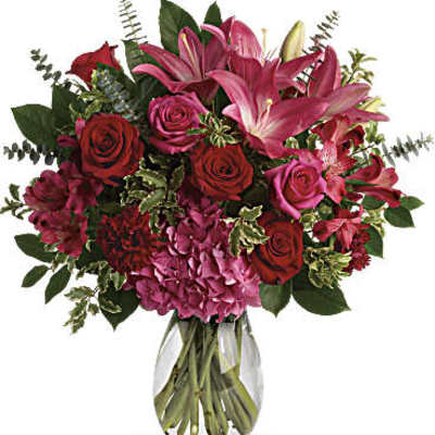 Arrangement of red roses, pink lilies, and hydrangeas in a clear glass vase