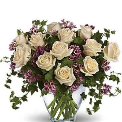 Arrangement of cream roses with small purple flowers in a clear glass vase