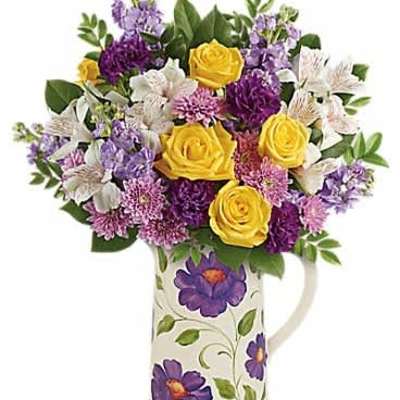 Yellow roses and purple flowers in a patterned ceramic pitcher with painted purple blooms