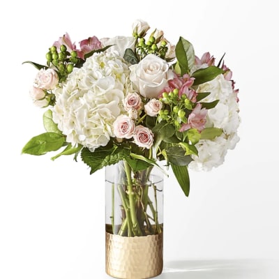 White hydrangeas and pale pink roses in a glass vase with a gold base