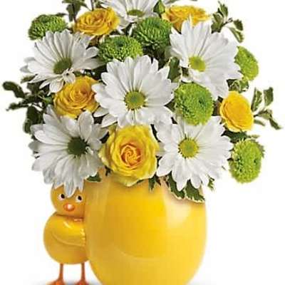 White daisies and yellow roses in a yellow egg-shaped vase with a small chick figure.