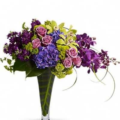 Tall glass vase with purple orchids, blue hydrangeas, green orchids, and pink roses in an asymmetrical arrangement