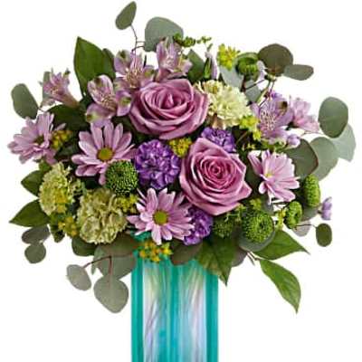 Lavender roses and mixed purple and green blooms arranged in a tall turquoise glass cylinder vase