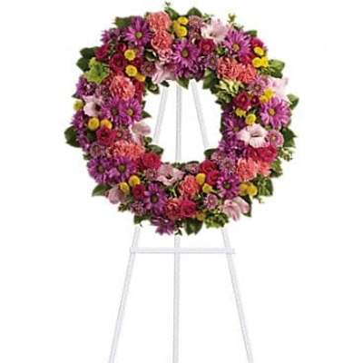 Standing wreath of pink, purple, and yellow flowers on a white easel