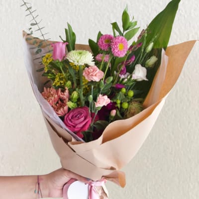 Hand-tied bouquet of pink, white, and yellow flowers wrapped in tan paper