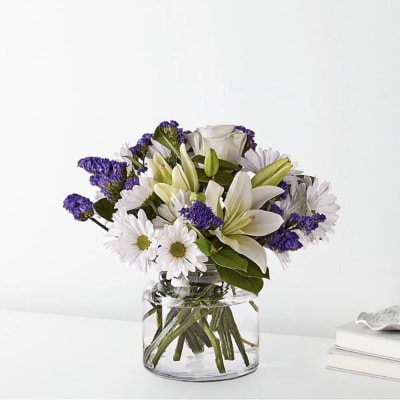 White lilies and daisies with purple filler in a clear glass vase