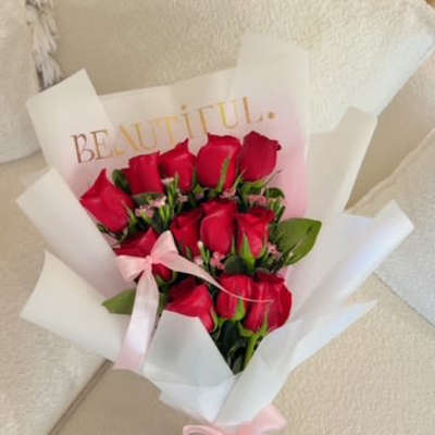 Bouquet of red roses wrapped in white paper with a pink ribbon