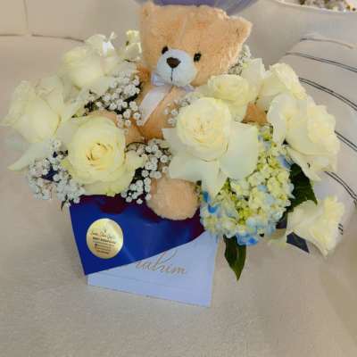 Teddy bear in white roses with a blue welcome balloon