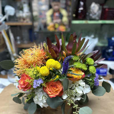 Mixed bouquet with orange roses, yellow mums, and white hydrangea in a low container