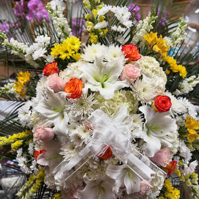 Large white floral spray with lilies, roses, and daisies tied with a white ribbon