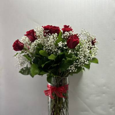 Red roses and baby's breath in a clear glass vase with a red ribbon