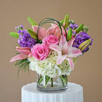 Pink roses and lilies arranged with purple flowers in a glass vase