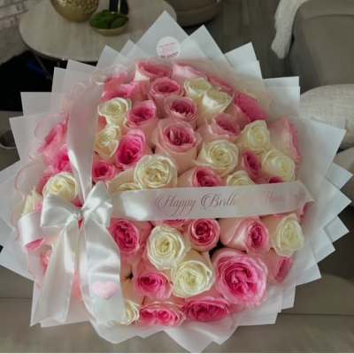 Pink and white rose bouquet wrapped in white paper with a satin bow