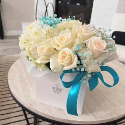 Cream roses and white flowers in a white gift box with a blue ribbon