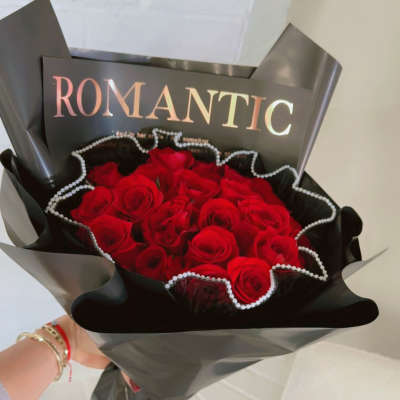 Bouquet of red roses wrapped in black paper with a "ROMANTIC" card
