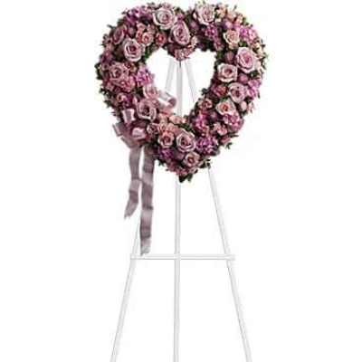 Heart-shaped pink rose standing wreath on a white easel with a lavender ribbon bow