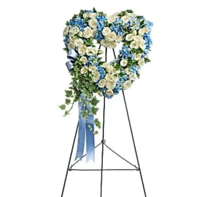 Heart-shaped standing wreath of white roses and blue flowers with trailing ivy on a metal easel