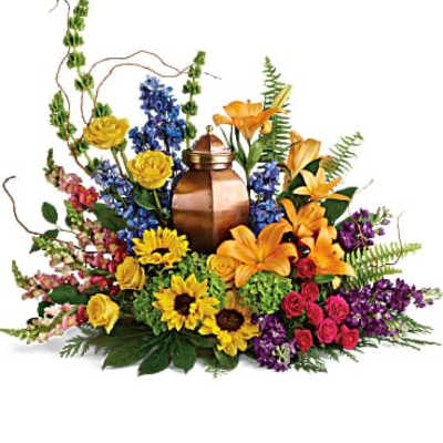 Colorful sympathy arrangement with a copper urn framed by yellow, orange, and purple flowers.