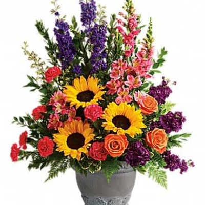Tall mixed arrangement with sunflowers, orange roses, pink blooms and purple flowers in a gray urn vase