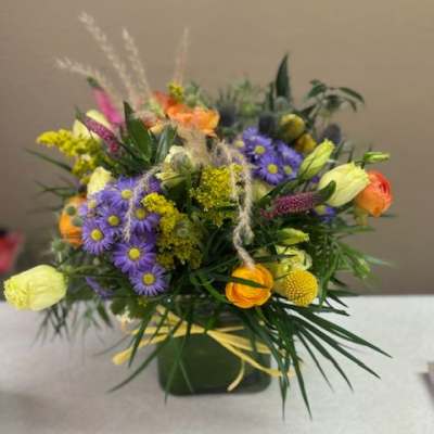 Mixed bouquet of purple daisies and orange blooms in a green container