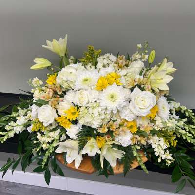 Large white floral arrangement with lilies, roses, and yellow accents in a low container