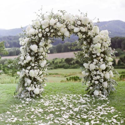 White floral arch outdoors with petals scattered on grass