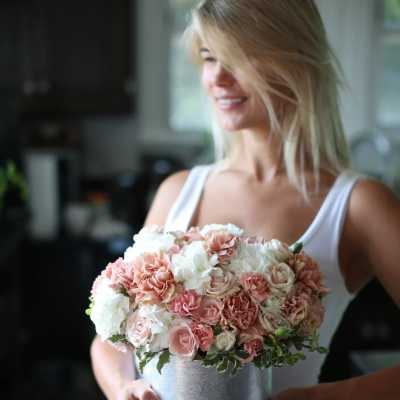 Woman holding a round pink and white rose bouquet in a silver bucket