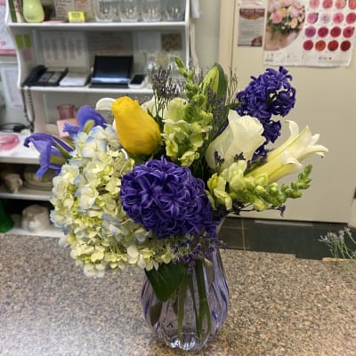 Mixed bouquet of purple, yellow, and white flowers in a glass vase