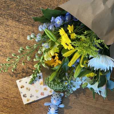 Mixed bouquet with yellow and blue flowers, plus a small crocheted teddy bear