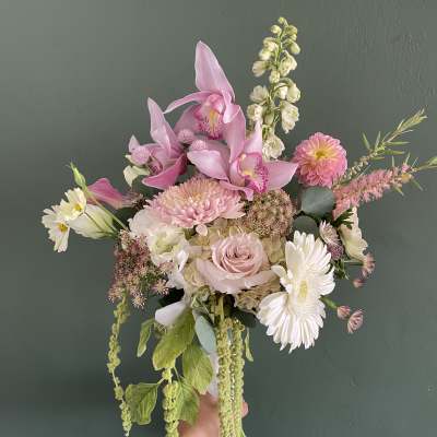 Handheld bouquet of pink orchids, roses, and white daisies