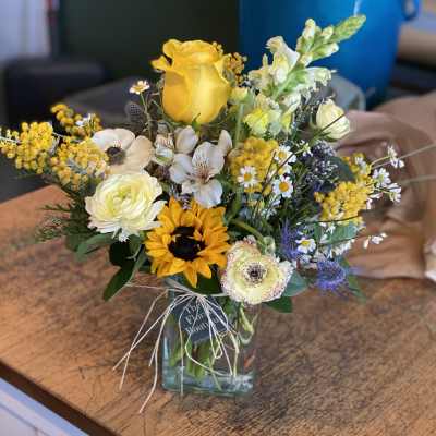 Mixed bouquet with yellow roses, sunflower, and white blooms in a glass vase